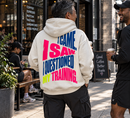 Questioned My Training cream hoodie worn by an athlete outside a coffee shop after training, featuring bold statement back artwork inspired by race day and training humor.