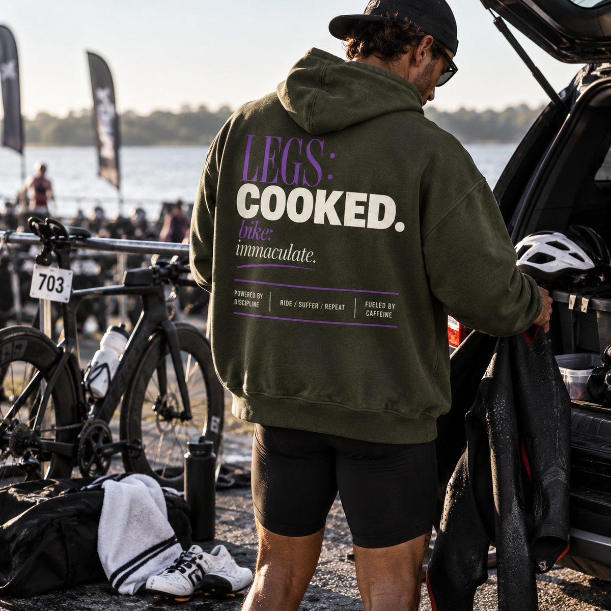 Race Scoop Legs Cooked olive hoodie worn by a triathlete in the transition area, featuring bold cycling inspired back artwork after a demanding bike leg.