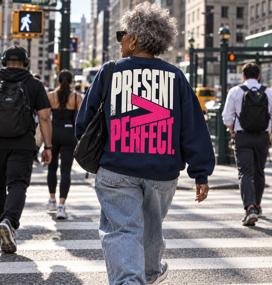 Race Scoop Present Over Perfect navy crewneck worn in an everyday city setting, featuring bold statement back artwork celebrating showing up over perfection.