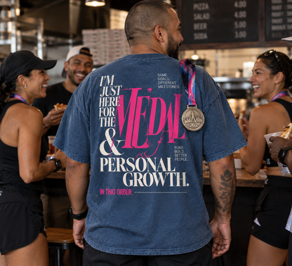 Race Scoop Medal and Personal Growth blue graphic tee worn by a marathon finisher celebrating with friends after the race, featuring statement back artwork and a finisher medal.