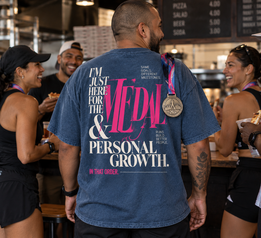 Race Scoop Medal and Personal Growth blue graphic tee worn by a marathon finisher celebrating with friends after the race, featuring statement back artwork and a finisher medal.